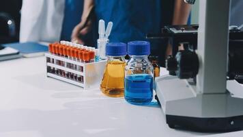 A group of people in lab coats standing around a table with a microscope video