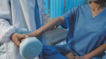 A woman in scrub clothes is holding a dumbbell video