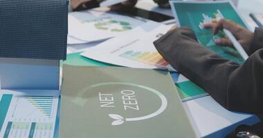 People sitting at a table with papers and a net zero sign video