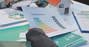 A group of people sitting around a table with papers and a house video