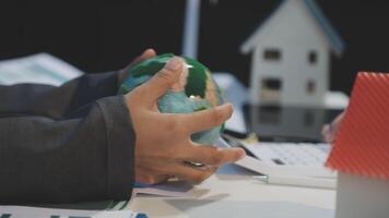 A person holding a globe on a desk with a house and a house video