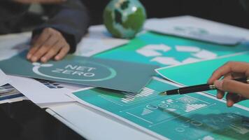 A group of people sitting at a table with papers and a green net zero logo video