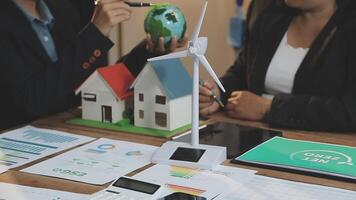 A group of people are sitting around a table with a wind turbine video