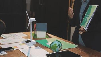 A man is standing at a table with papers and a wind turbine video