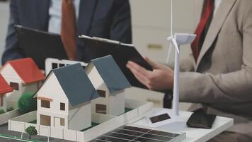 Two people are looking at a model of a house and a wind turbine video