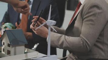 Businessman in suit and tie holding a paper model of a house and wind turbine video