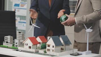 Two men in suits are holding a model of a house and wind turbines video