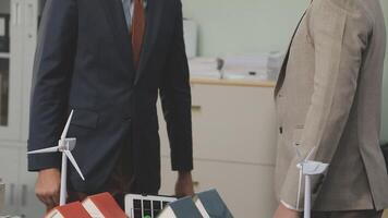 Two businessmen in suits standing next to a desk with wind turbines video