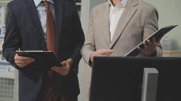 Two men in suits standing in front of a computer video