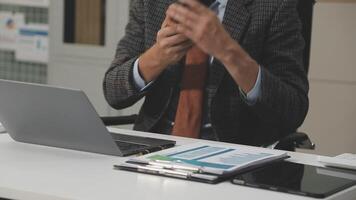 A man in a suit sitting at a desk with a laptop video
