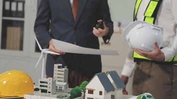 Two men in business attire standing next to a model of a house video