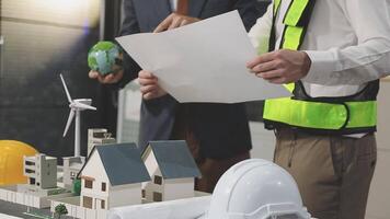 Two men in safety vests and hard hats are looking at a model of a house video
