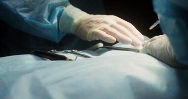 Medical instruments for the operation lie at the hand of the surgeon on the patient covered with a sheet. Close-up of a surgeon's hands with a scalpel. 4k, red komodo video