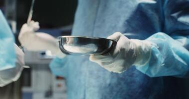 Close-up of the hands of a surgeon's assistant with a bowl for biological debris during an operation. No face, medical team work in operating room. in 4k, red komodo video
