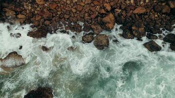 Top view of the seashore, foam waves crashing on a rocky shore, drone video