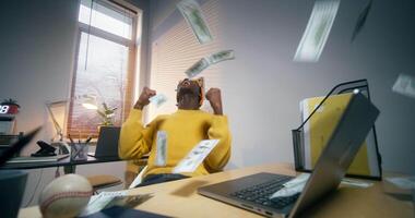 A man in informal clothes is typing on laptops in the office, when dollar bills start falling on him, he laughs and rejoices video