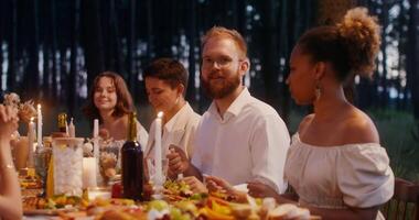 Guests laugh and talk while sitting at a beautifully served festive table in the open air. A man lights candles video