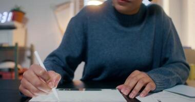 A woman wearing headphones smiles while drawing on a graphics tablet with a stylus, sitting at a desk in the office video