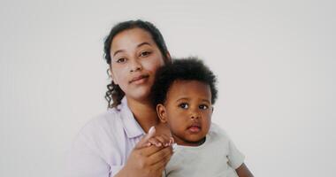 Mom and daughter of African-American appearance smile while looking at the camera posing on a white studio background video