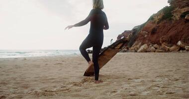 A man in a diving suit does a warm-up standing on the seashore and looking into the distance. Rear view, no face, surfboard standing nearby video