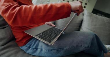 A woman opens a laptop sitting on the couch and smiles starting typing. The flips from vertical to horizontal video