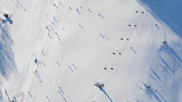 Aerial view of ski slope with skiers and lifts, ski tracks on snow and shadows of trees video