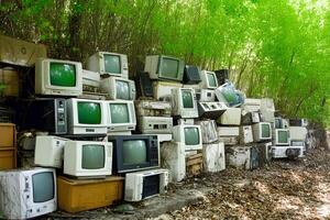A collection of old, discarded televisions scattered on the forest floor, showcasing environmental pollution in a natural setting photo