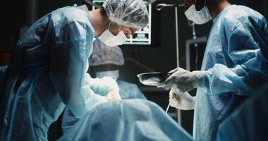 A team of young surgeons, dressed in disposable sterile clothing, performs an operation to remove a tumor in a modern operating room. in 4k, red komodo video