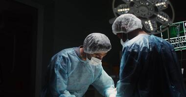 A team of surgeons wearing disposable caps and medical face masks perform laparoscopic surgery in a well-equipped operating room. in 4k, red komodo video