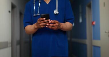 A male doctor with a phonendoscope around his neck is typing on a mobile phone while walking along an empty clinic corridor. No face, unrecognizable person. in 4k, red komodo video
