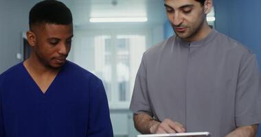 Two doctor colleagues of different nationalities stop while walking along the corridor of a medical clinic and look at a digital tablet. movement from faces to hands. in 4k, red komodo video