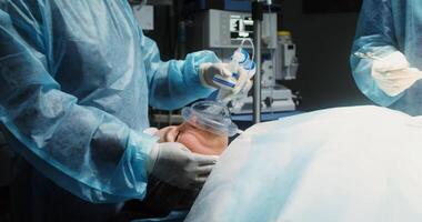 A young female patient with an oxygen mask on her face lies on the operating table during a surgical operation. Coordinated work of medical personnel in operating room. in 4k, red komodo video