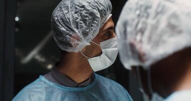 Close-up of the focused face of a surgeon in a medical mask and a disposable cap on his head during an operation in the operating room. 4k, red komodo video