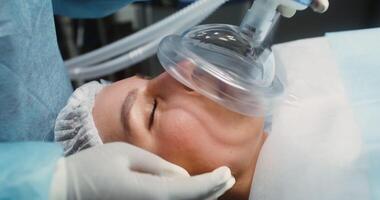 Close-up of the face of a young woman patient with closed eyes, with an oxygen mask on her face, lying on the operating table during a surgical operation. in 4k, red komodo video