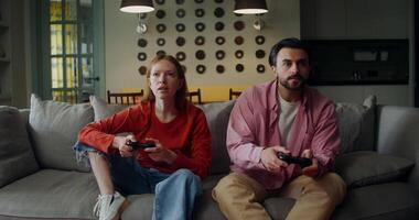 A man and a woman are intently playing games with joysticks and hugging, rejoicing at victory, sitting on the couch at home video