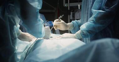 A team of surgeons dressed in sterile clothing performs a surgical operation in a modern, well-equipped operating room. Close-up of doctors' hands in disposable gloves. in 4k, red komodo video