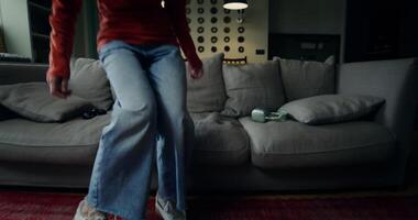 A young woman in casual clothes sits on the sofa, puts on headphones and starts gambling in a game using a joystick video