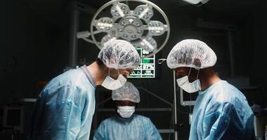 A team of doctors talk among themselves, bending over a patient, during a surgical operation. the patient is not in the frame. in 4k, red komodo video