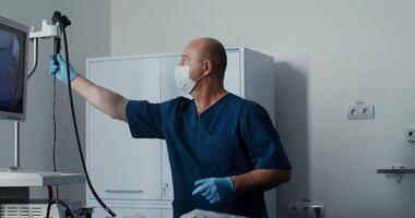 A gastroenterologist takes a joystick to control a microcamera to examine the large intestine of a patient lying on a bed, dressed in a disposable surgical suit. 4k , red komodo video