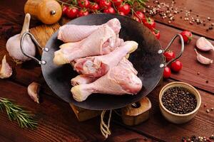 Fresh chicken drumsticks and ingredients arranged on a rustic wooden table in preparation for cooking photo