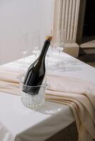 Elegant champagne bottle chilling in a crystal ice bucket with flutes beside on a white table photo