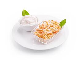 Fresh carrot salad with yogurt dressing served on a white plate with mint leaves at a kitchen table photo