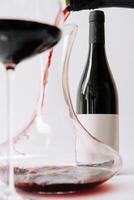 Elegant red wine being poured into a decanter with a glass next to it on a simple white background photo