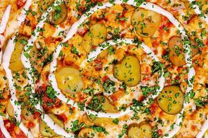 Unique pizza topped with pickles, herbs, and creamy sauce presented in a spiral pattern on a rustic wooden table photo