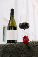 Elegant red wine bottle and glass with a rose during a romantic evening setting photo
