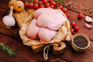 Fresh chicken breasts arranged with cherry tomatoes, garlic, and spices on a wooden table top photo