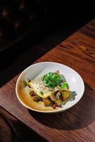 Grilled fish served with roasted potatoes and herbs on a rustic wooden table in a cozy dining setting photo