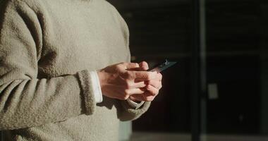 A man dressed in a warm sweater is typing a message on his phone using the Internet while walking around the city. Close-up of male hands, no face. in 4k, red komodo video