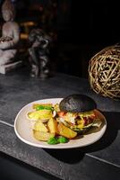 Gourmet burger with black bun and crispy potatoes served in a cozy restaurant setting at night photo