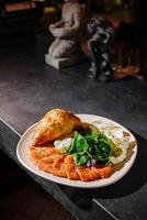 Deliciously arranged plate of smoked salmon, salad, and croissant served on a dark countertop in a cozy setting photo